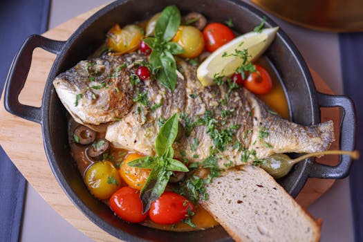 Delicious roasted fish with basil, tomatoes, olives, and lemon slice in rustic presentation.